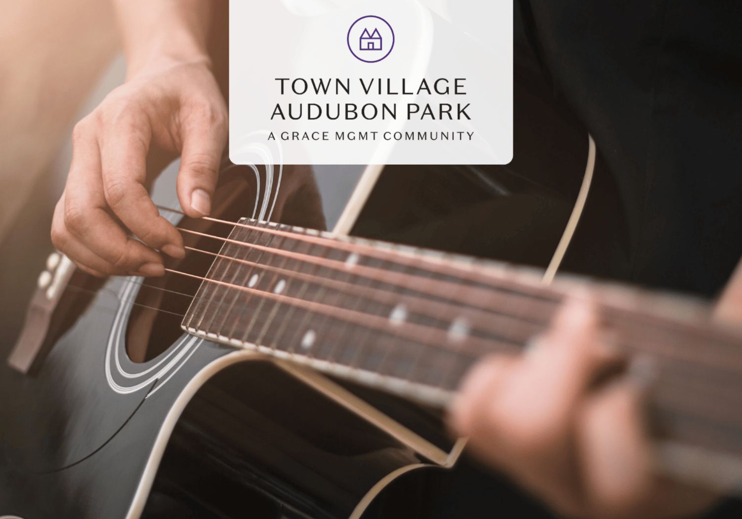 Close-up of a person strumming an acoustic guitar with a translucent logo overlay reading 'Town Village Audubon Park'