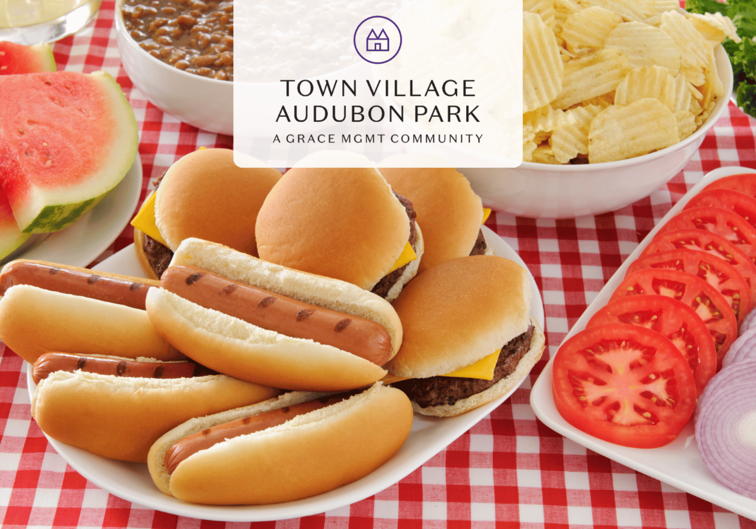 Picnic spread: hot dogs in buns, cheeseburgers, potato chips, watermelon wedges, sliced tomatoes on a red-and-white check tablecloth with a centered Town Village Audubon Park logo overlay.