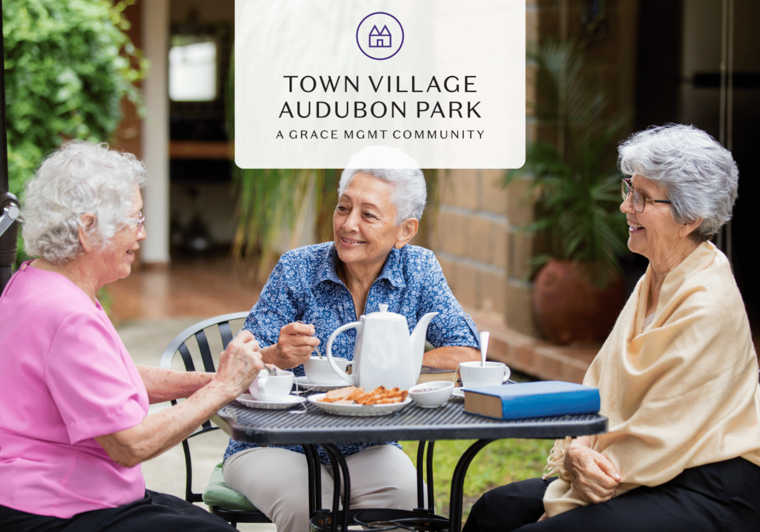 Three elderly women sit around an outdoor table, chatting over tea and cookies, with a Town Village Audubon Park sign overlayed above them.