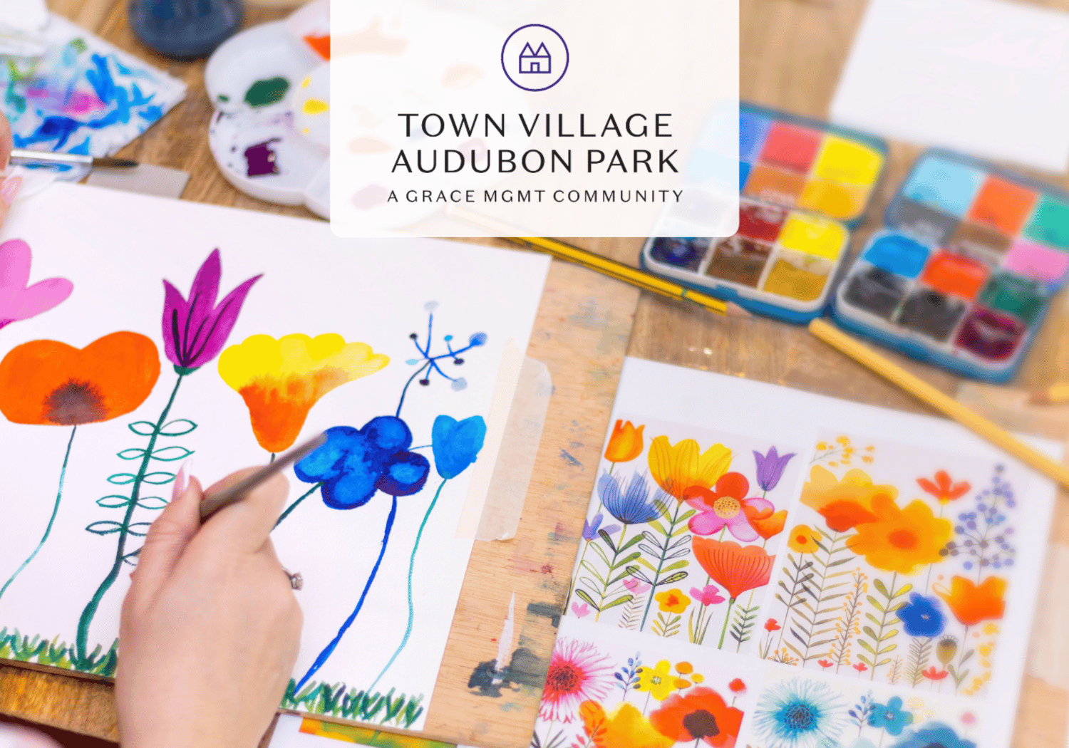 Art workshop scene with bright watercolor flowers being painted, paints and brushes on a wooden table; logo overlay reads Town Village Audubon Park.